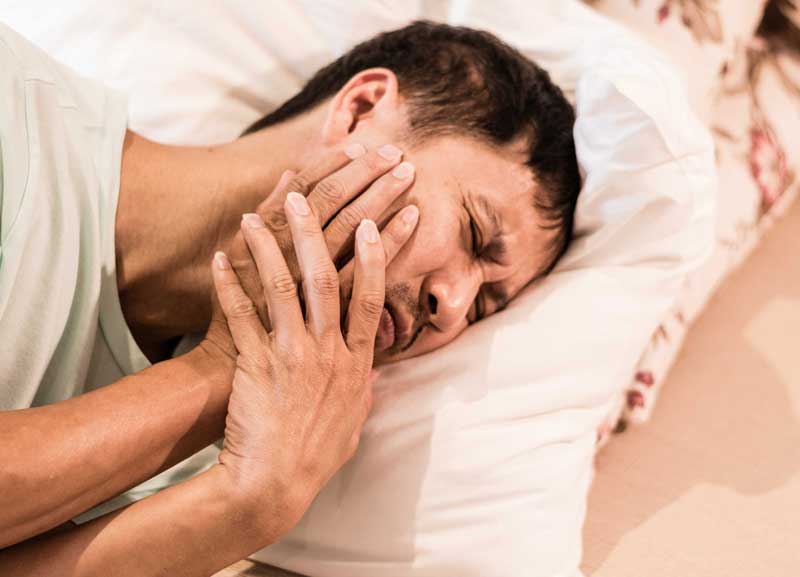 a man lying in bed is suffering from his jaw pain